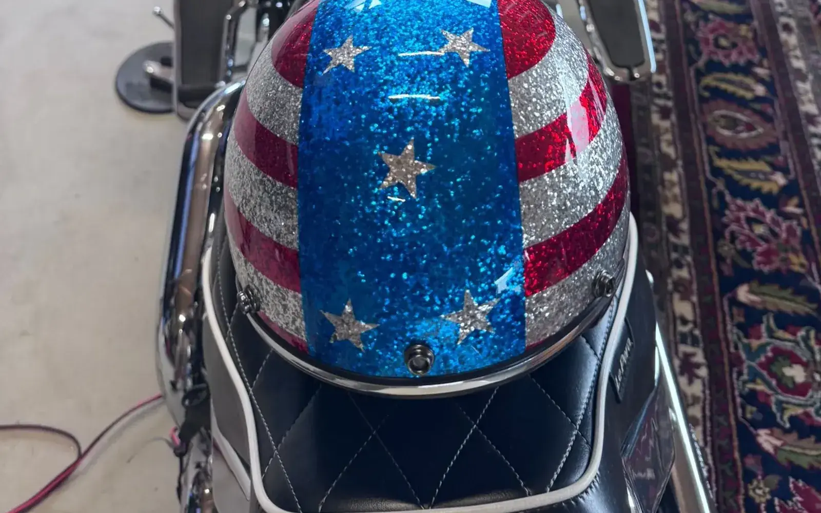Glitzerhelm im Stars-and-Stripes-Design auf der Sitzbank, dahinter Tank und Tacho einer Harley-Davidson